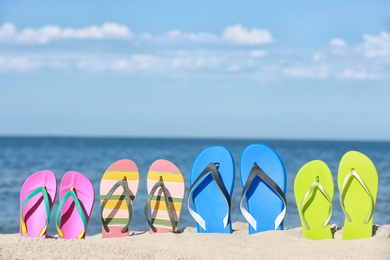 Composition with bright flip flops on sand near sea in summer. Beach accessories