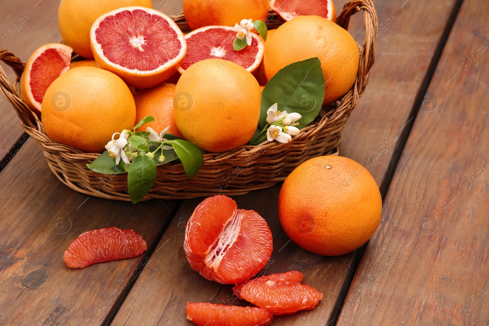 Photo of Wicker basket with fresh grapefruits and green leaves on wooden table