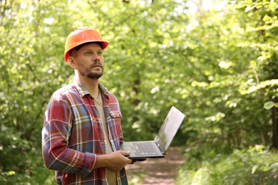 Forester with laptop examining plants in forest, space for text