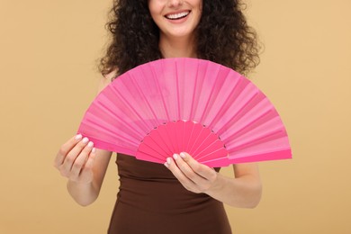 Photo of Woman holding hand fan on beige background, closeup