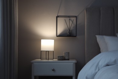 Photo of Stylish lamp and candles on white nightstand in bedroom