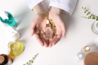 Dermatologist with bottle of essential oil at white table, top view. Development and testing