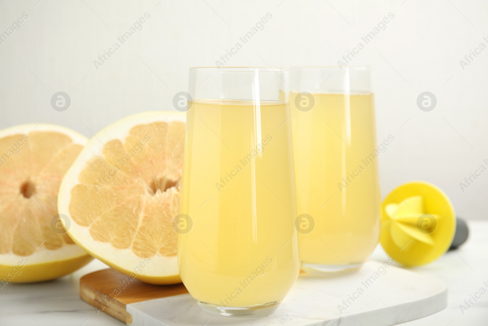 Photo of Glasses of fresh pomelo juice and fruit on white table