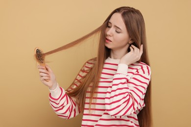Photo of Upset woman brushing her hair on beige background. Alopecia problem