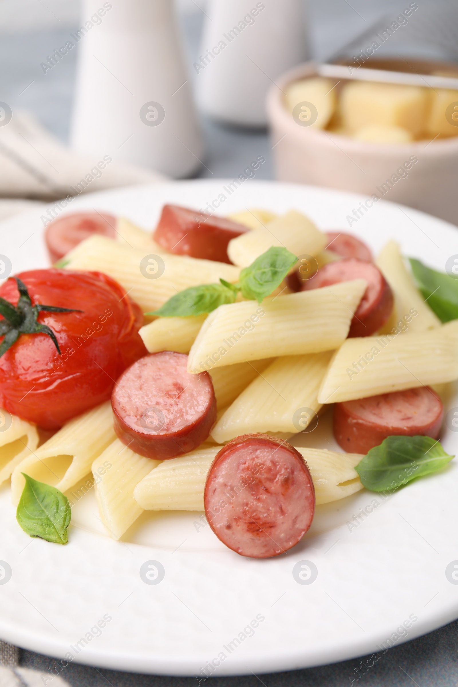 Photo of Tasty pasta with smoked sausage, tomato and basil on table, closeup