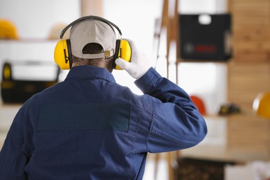 Photo of Worker wearing safety headphones indoors, back view. Hearing protection device