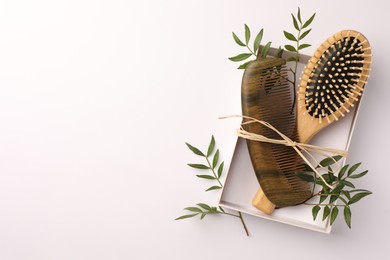 Wooden hairbrush, comb and green leaves on white background, top view. Space for text