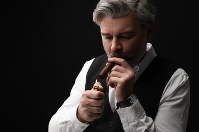 Photo of Bearded man lighting cigar on black background. Space for text