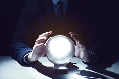 Photo of Businessman using crystal ball to predict future at table in darkness, closeup