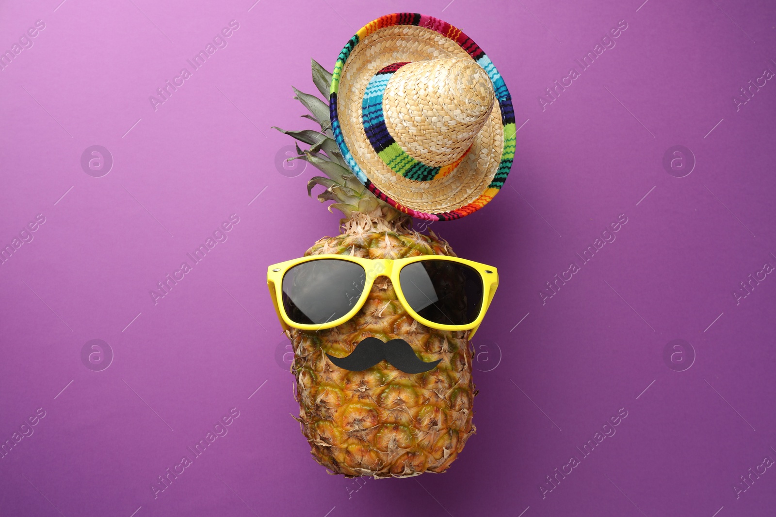 Photo of Pineapple with Mexican sombrero hat, fake mustache and sunglasses on purple background, flat lay