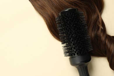 Photo of Professional round brush with brown hair strand on beige background, top view. Space for text