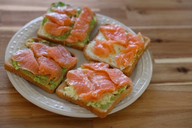 Photo of Sandwiches with avocado spread and salmon on wooden table, closeup