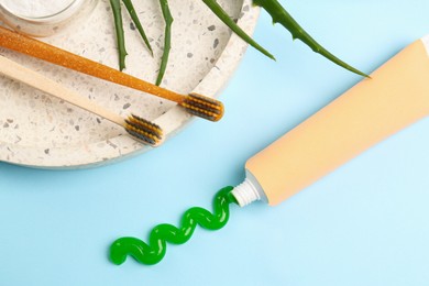 Tube of toothpaste, toothbrushes and fresh aloe on light blue background, flat lay