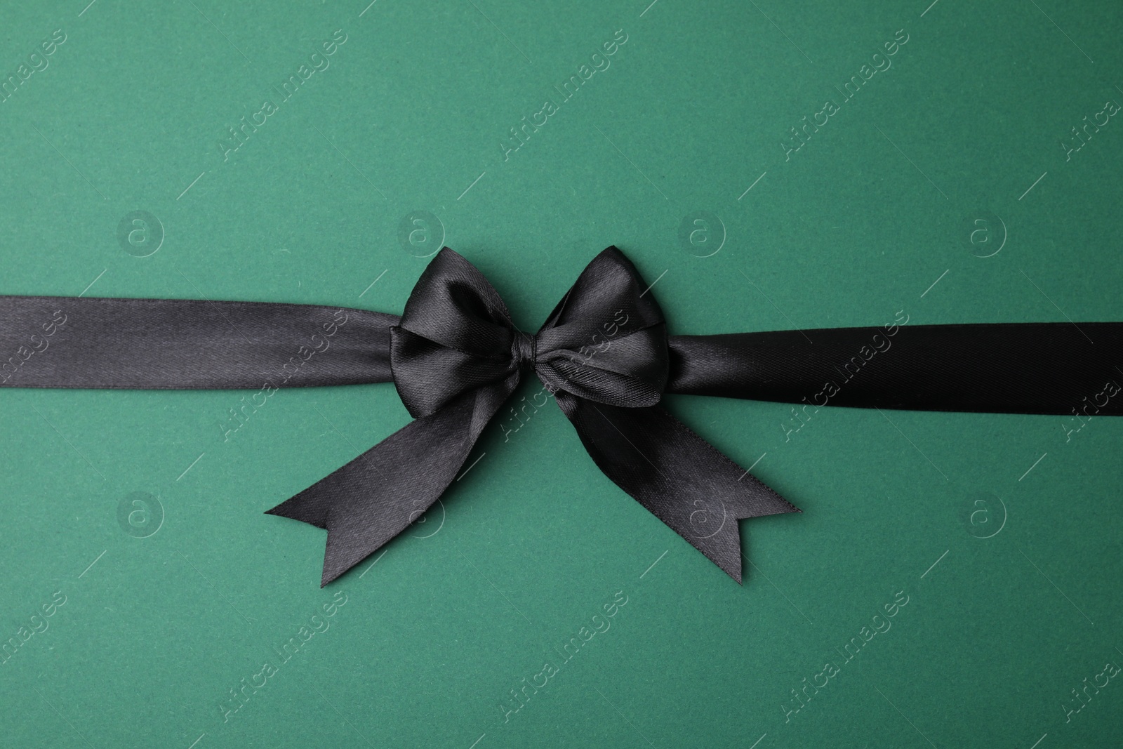 Photo of Black satin ribbon with bow on green background, top view