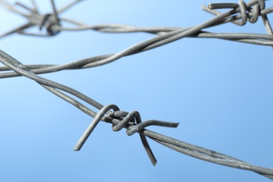 Photo of Metal barbed wire on light blue background, closeup