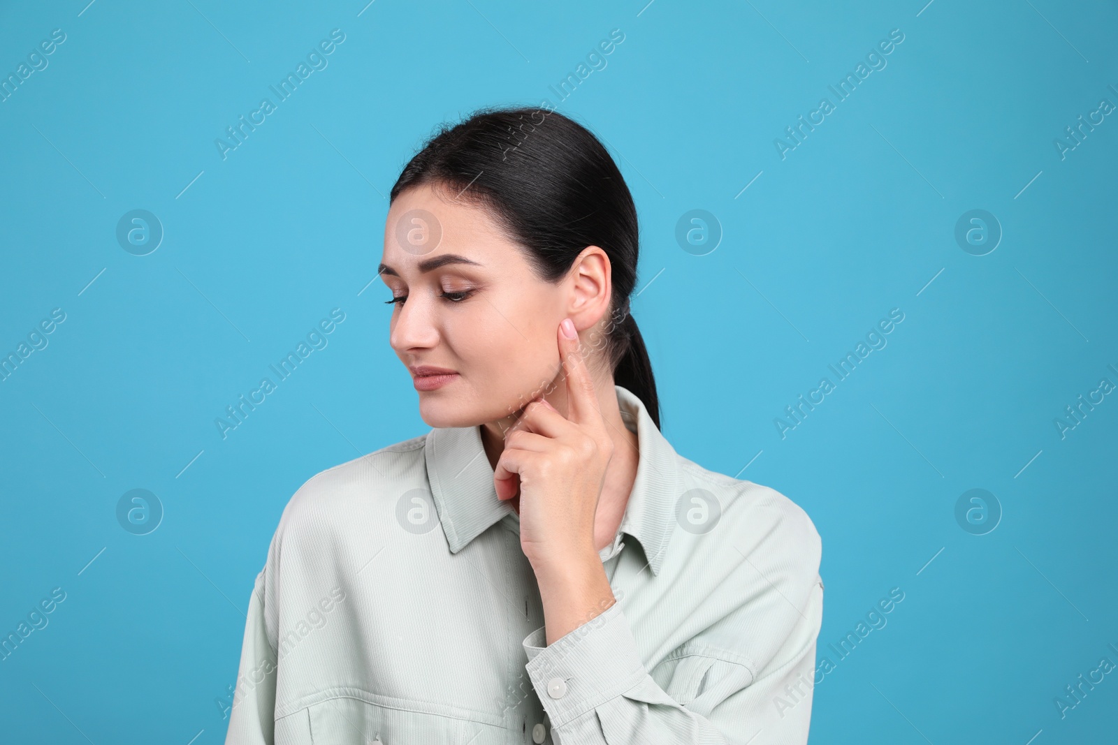 Photo of Young woman pointing at her ear on light blue background