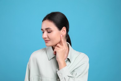 Photo of Young woman pointing at her ear on light blue background