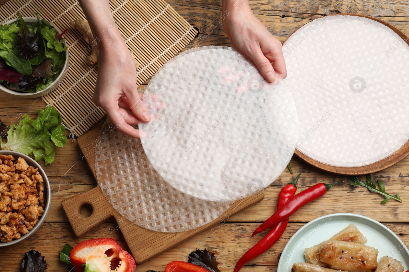 Photo of Woman making tasty spring roll at wooden table, top view