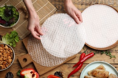 Photo of Woman making tasty spring roll at wooden table, top view