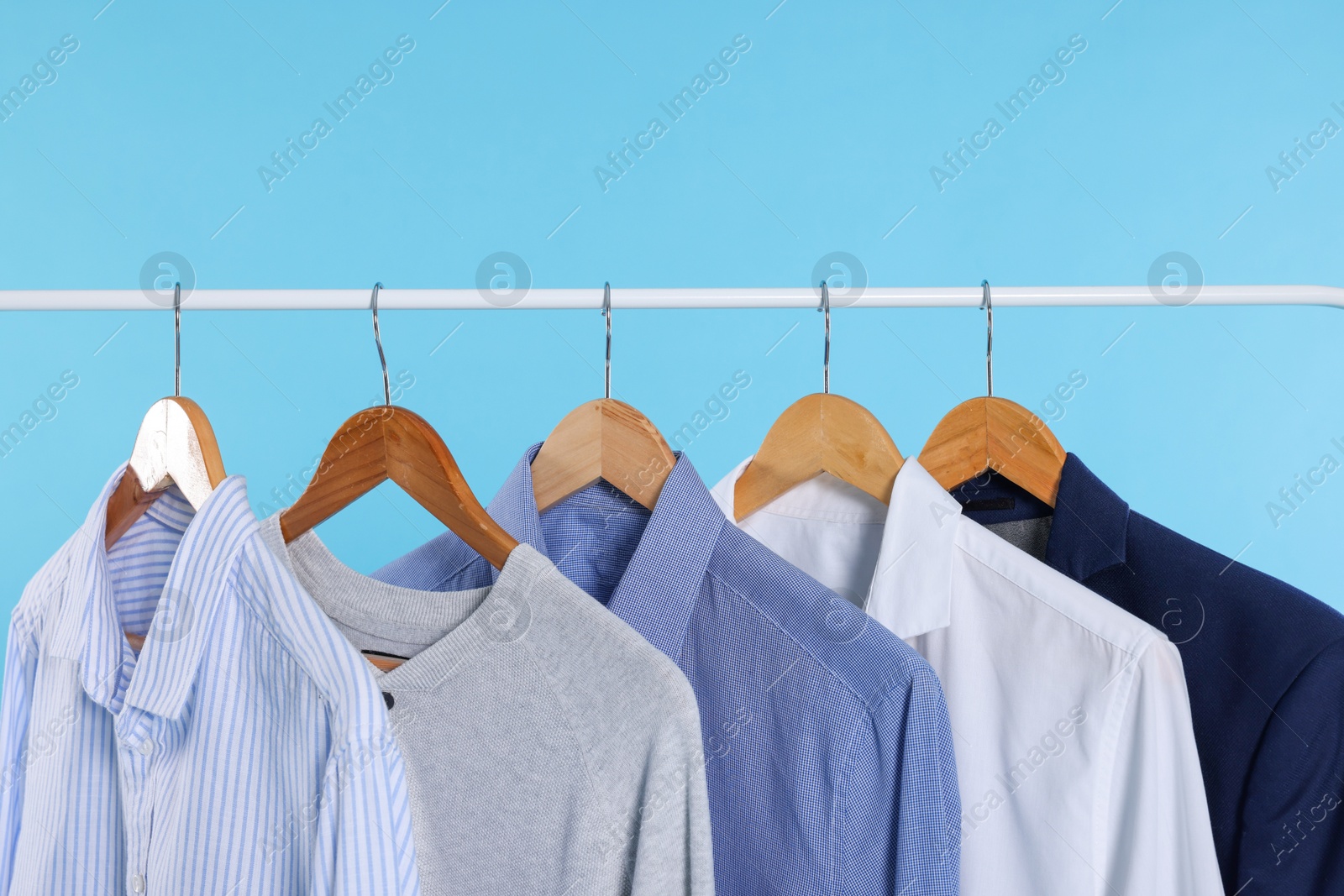 Photo of Rack with stylish clothes on wooden hangers against light blue background