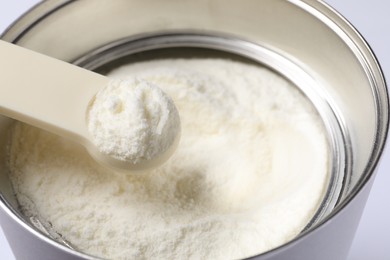 Photo of Scoop of powdered infant formula over can, closeup. Baby milk