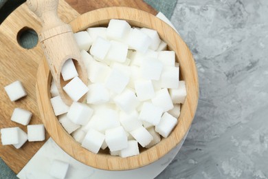 Photo of White sugar cubes in wooden bowl and scoop on grey table, top view. Space for text