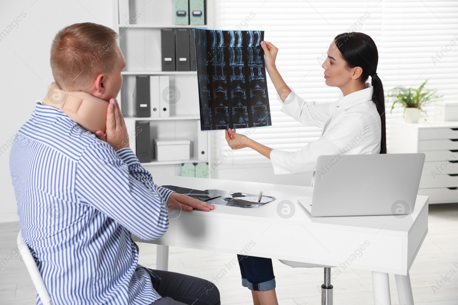 Photo of Doctor with neck MRI image consulting patient in clinic