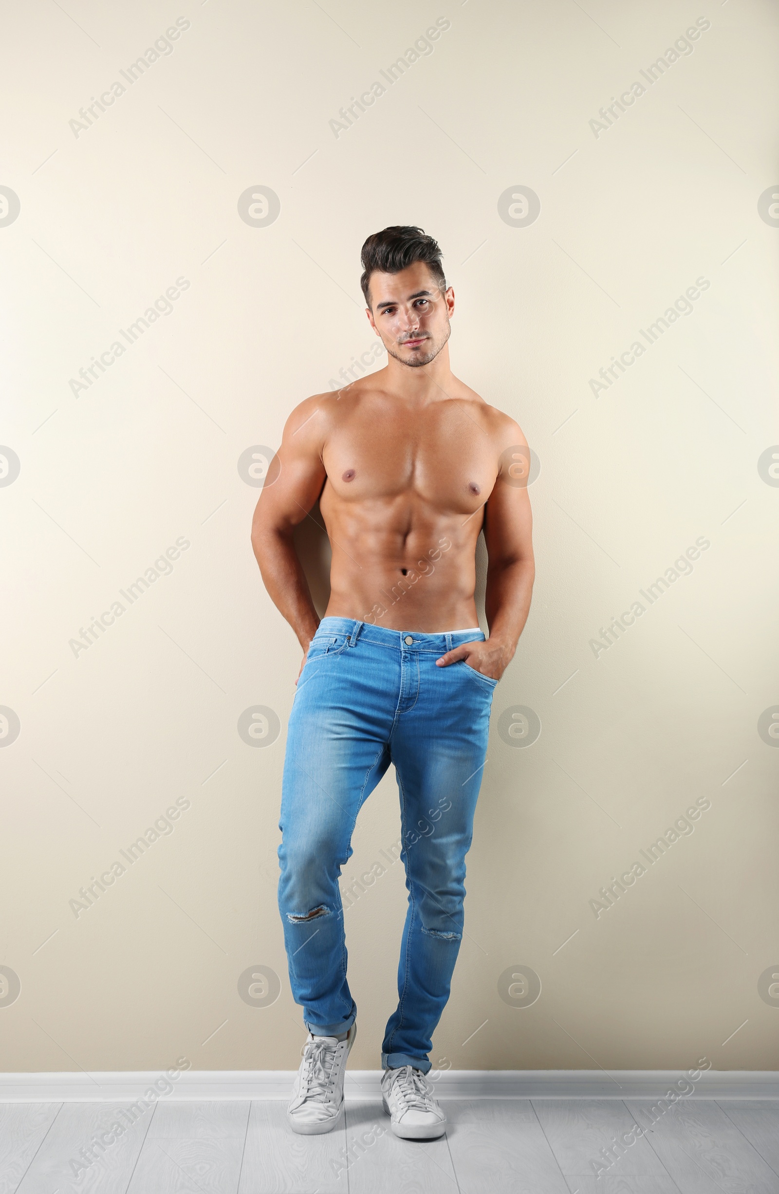 Photo of Shirtless young man in stylish jeans near light wall