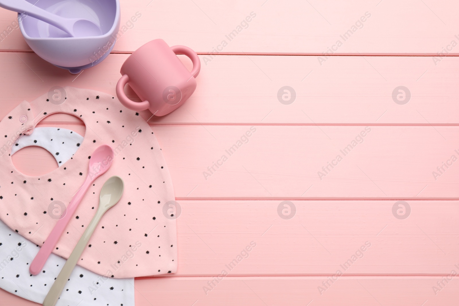 Photo of Flat lay composition with drool baby bibs and plastic dishware on pink wooden background. Space for text