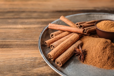 Photo of Plate with aromatic cinnamon powder and sticks on wooden table