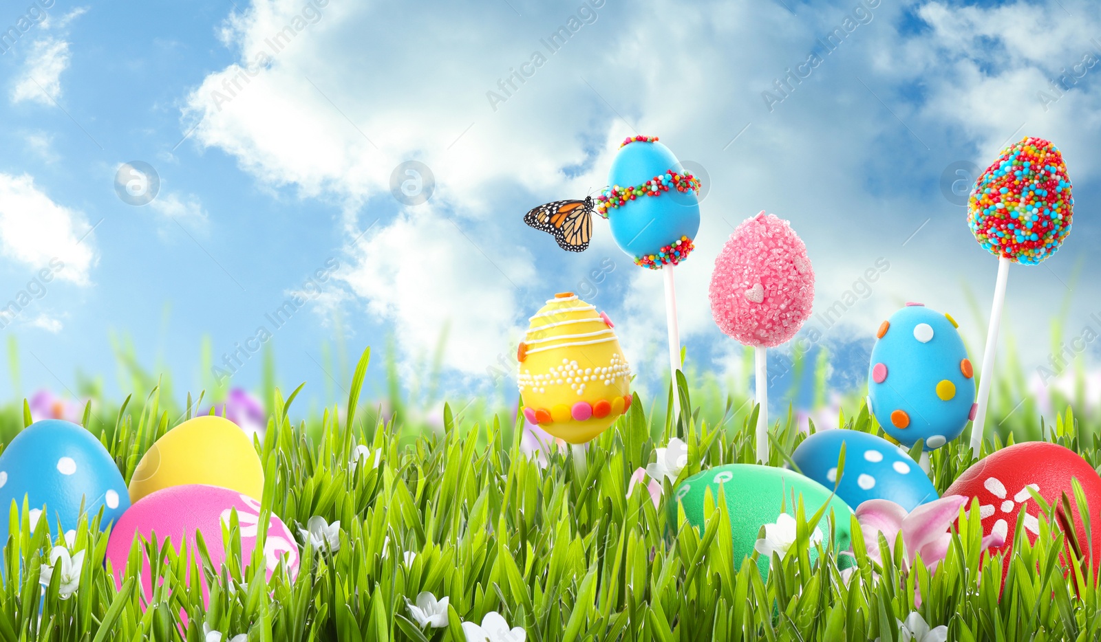 Image of Bright Easter eggs and cake pops in green grass against blue sky. Space for text