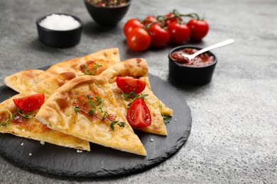 Cut delicious khachapuri with cheese, thyme, tomatoes and sauce on grey table
