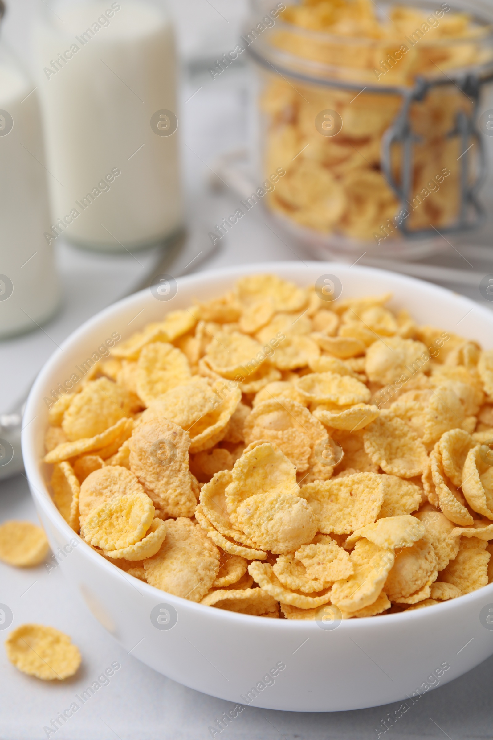 Photo of Tasty crispy corn flakes in bowl on white table, closeup. Breakfast cereal