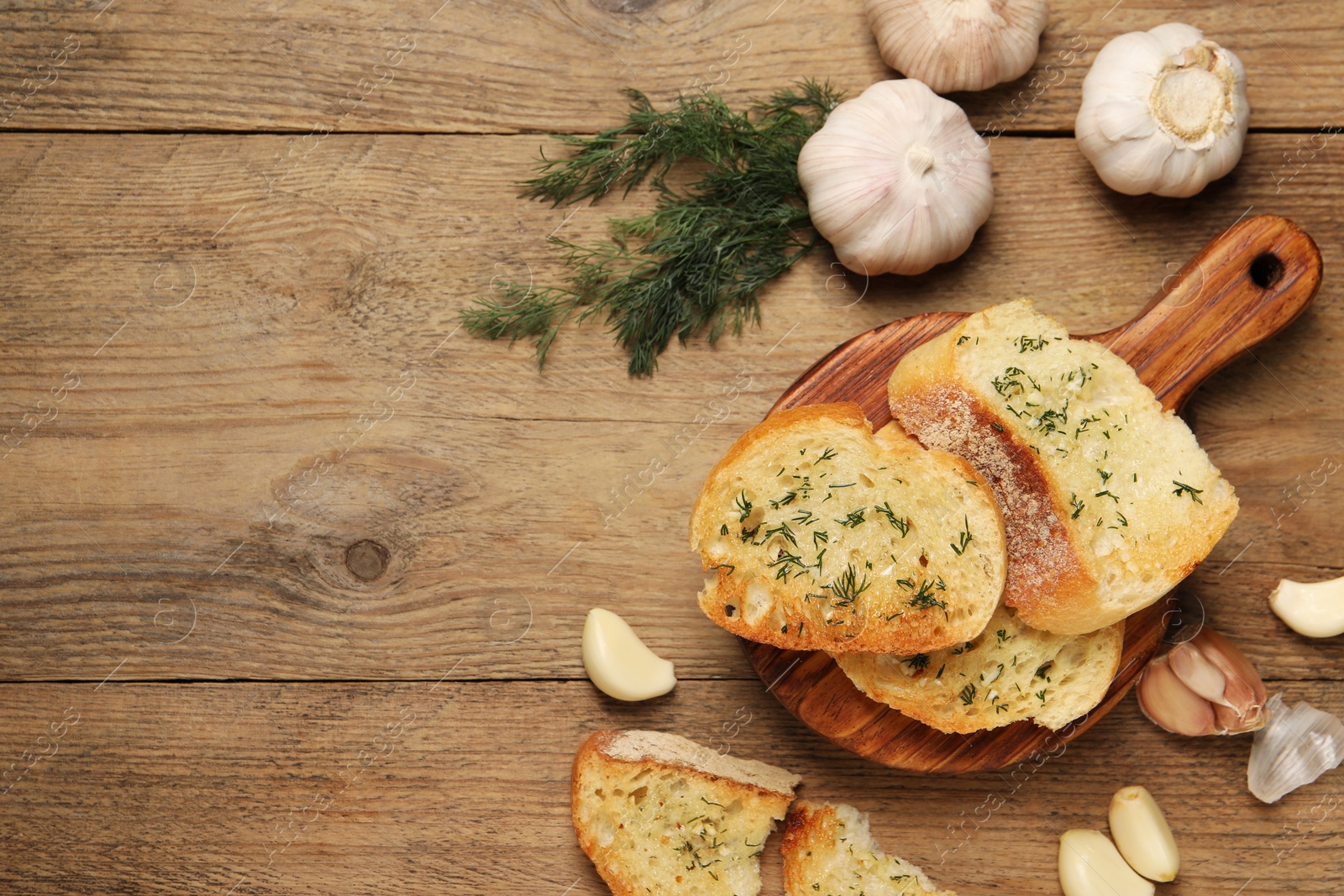 Photo of Tasty baguette with garlic and dill on wooden table, flat lay. Space for text