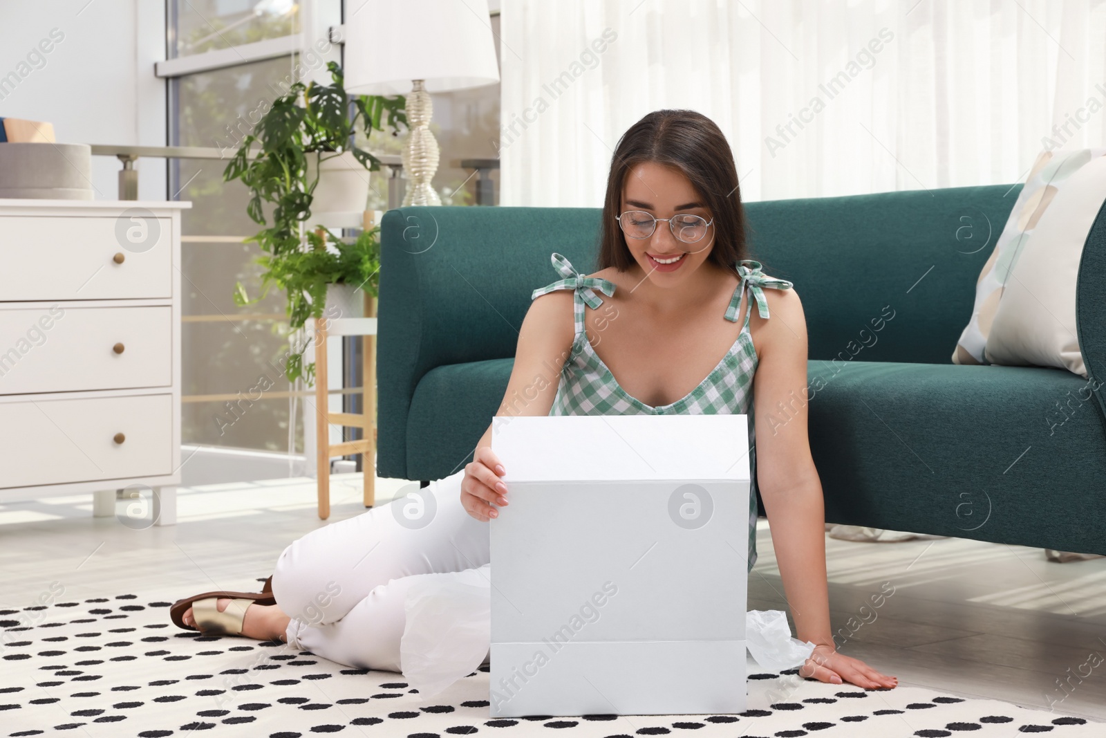 Photo of Happy young woman opening parcel on floor at home. Internet shopping