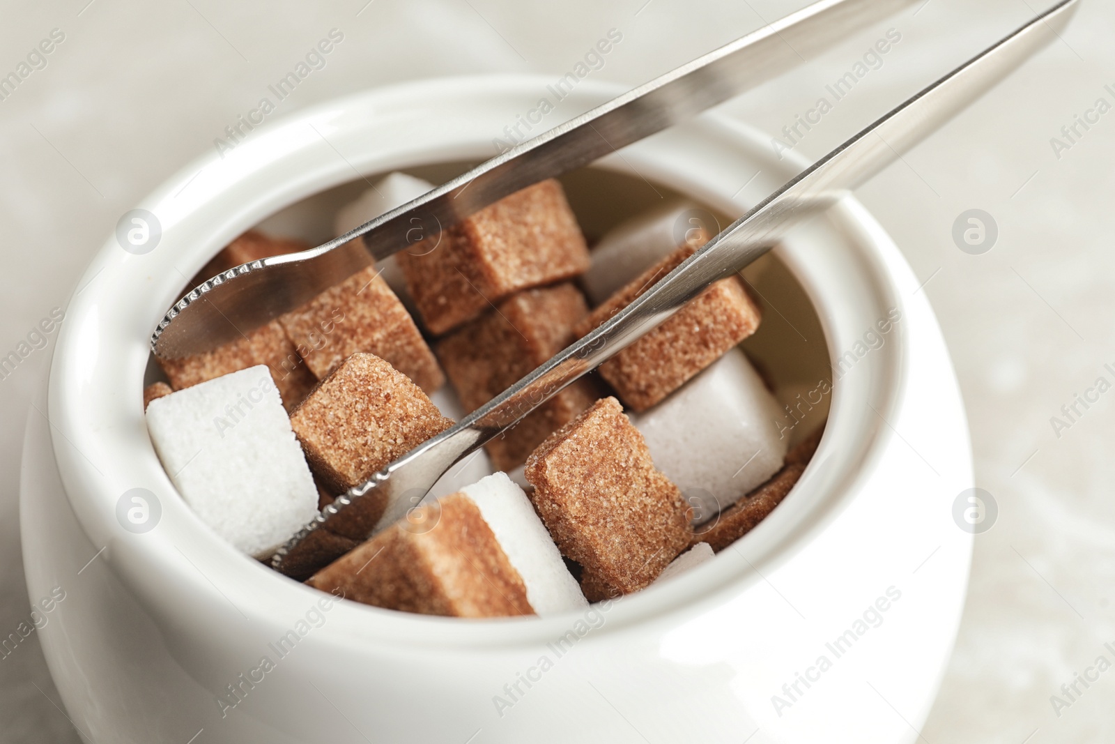 Photo of Different refined sugar cubes in bowl on light table, closeup