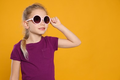 Girl wearing stylish sunglasses on orange background, space for text