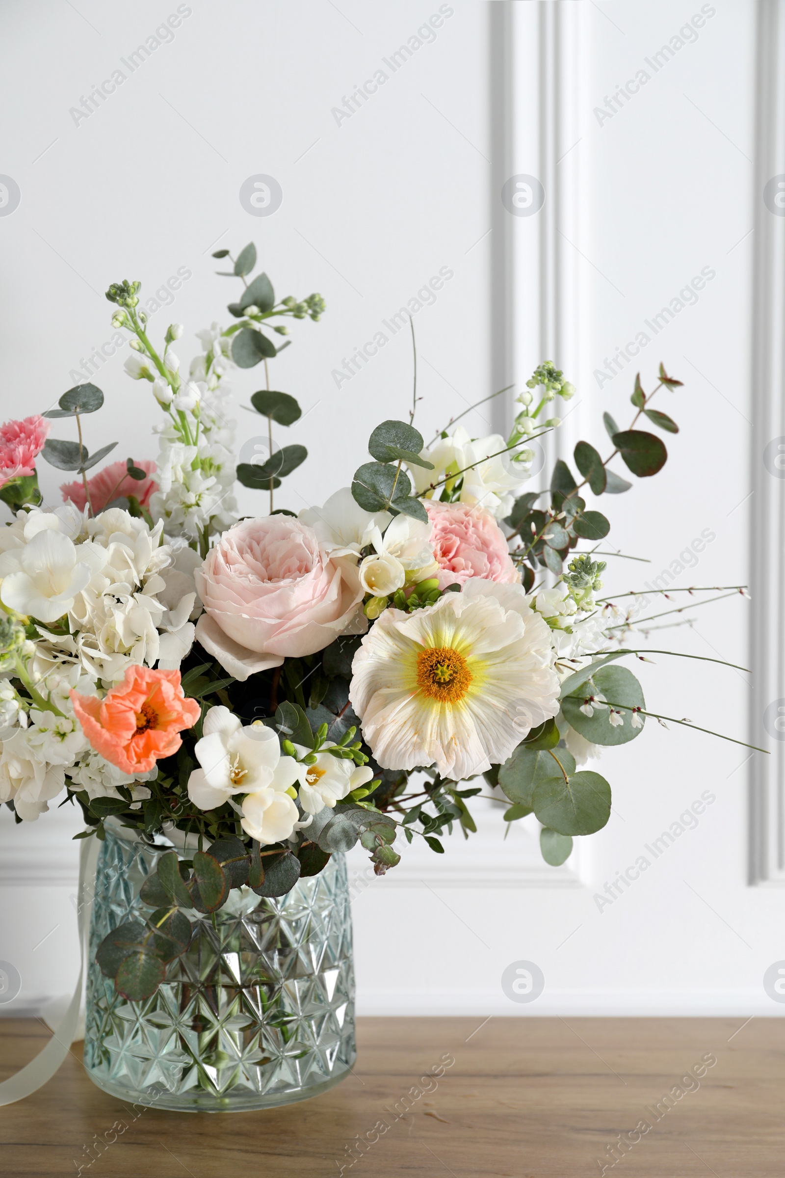 Photo of Bouquet of beautiful flowers in vase on wooden table near white wall