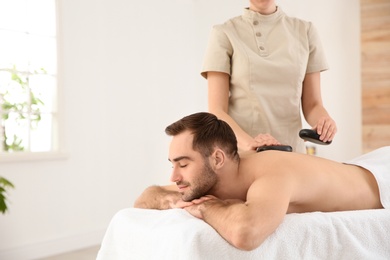 Handsome man receiving hot stone massage in spa salon