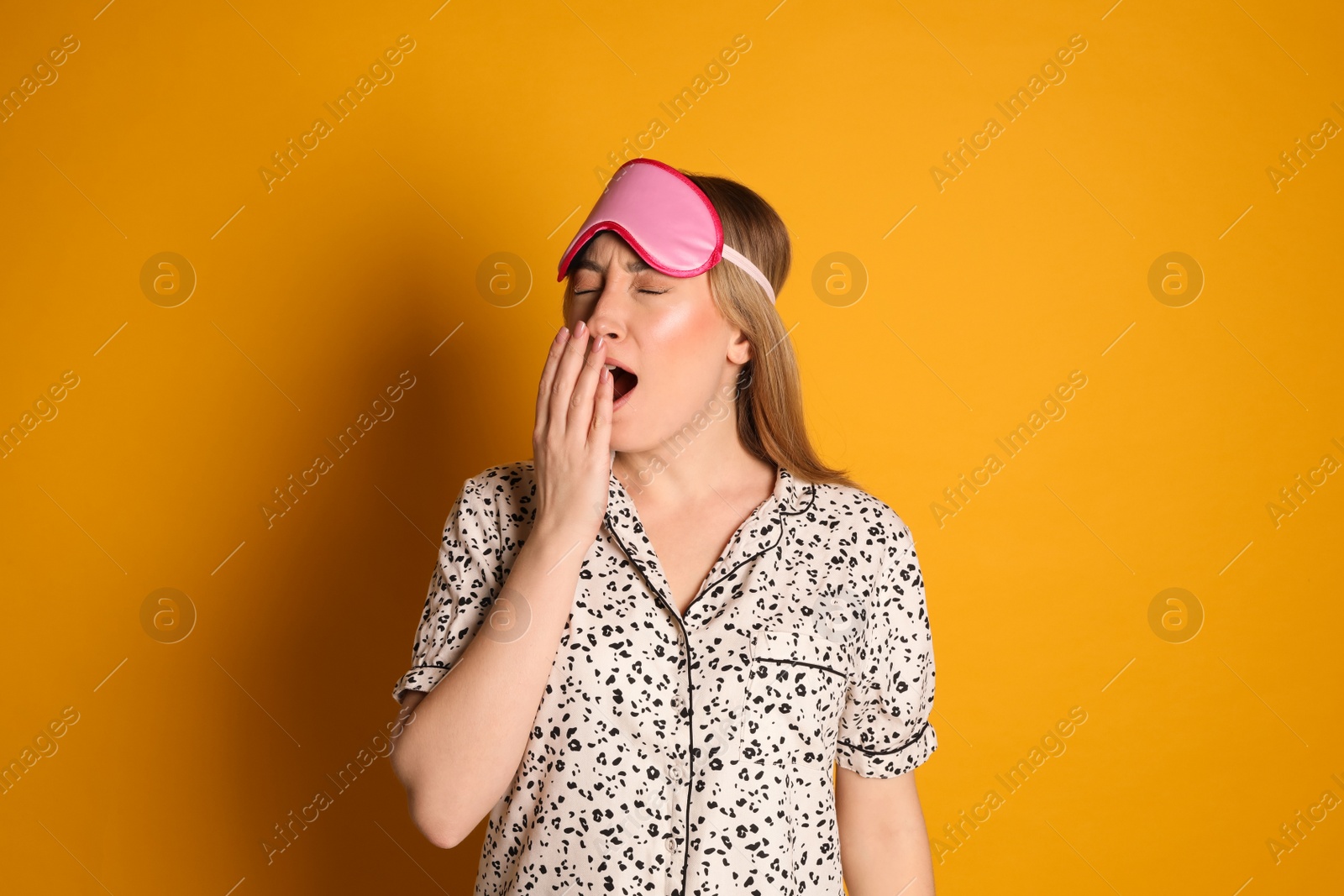 Photo of Young tired woman with sleeping mask yawning on yellow background