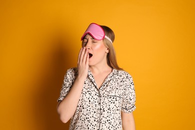 Young tired woman with sleeping mask yawning on yellow background