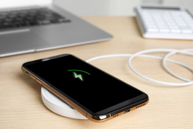 Photo of Mobile phone charging with wireless pad on wooden table, closeup