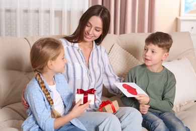 Photo of Cute little children presenting their mother with gifts on sofa at home