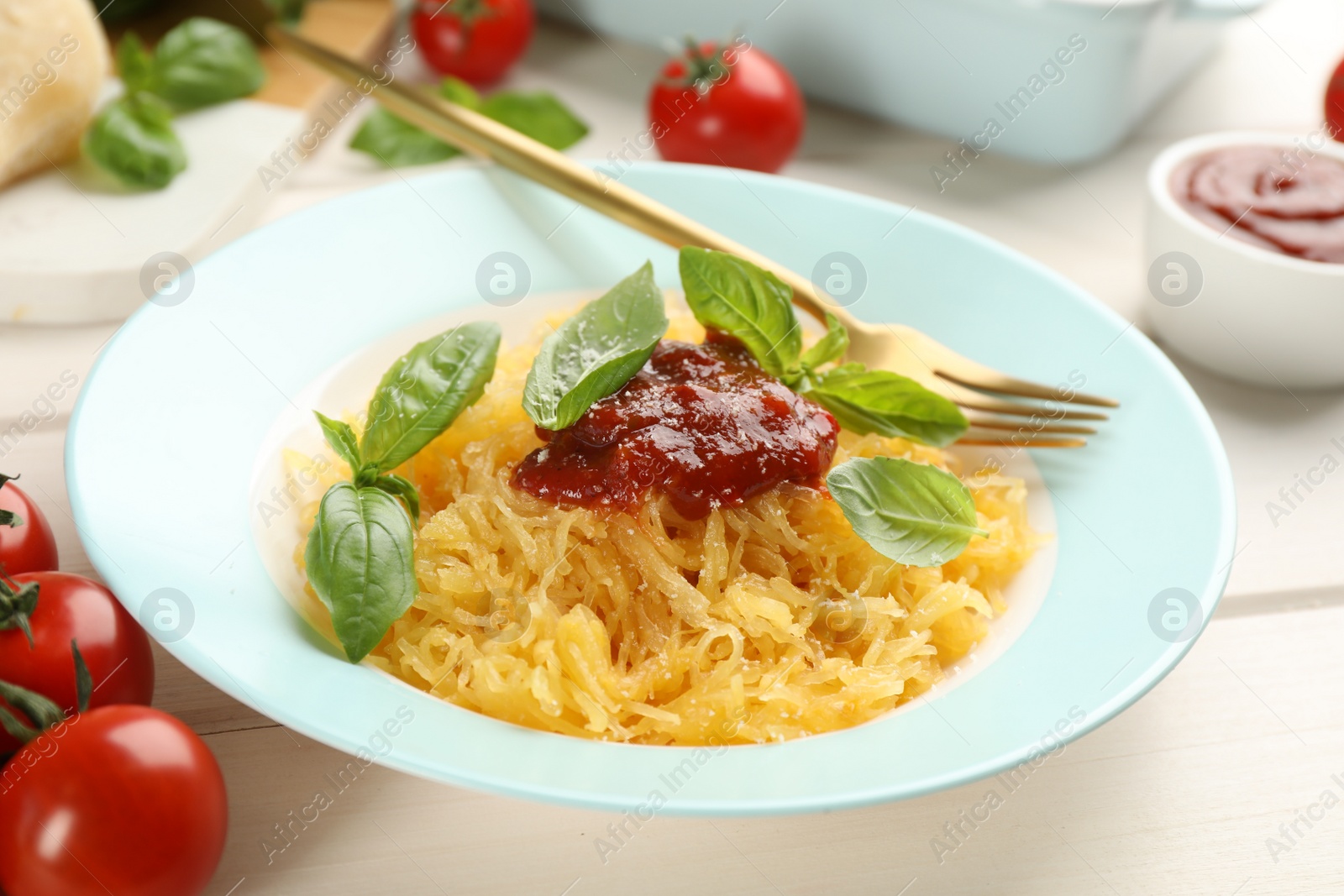 Photo of Tasty spaghetti squash with tomato sauce, cheese and basil served on white wooden table, closeup