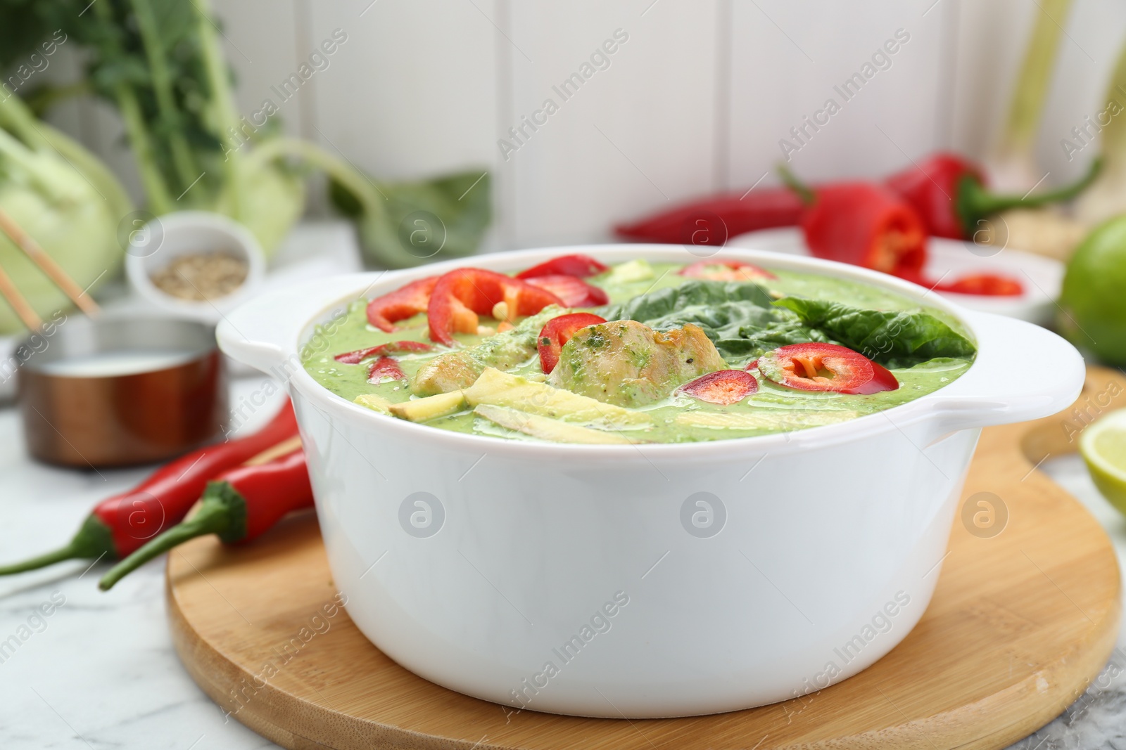 Photo of Saucepan with delicious green curry chicken soup on white marble table