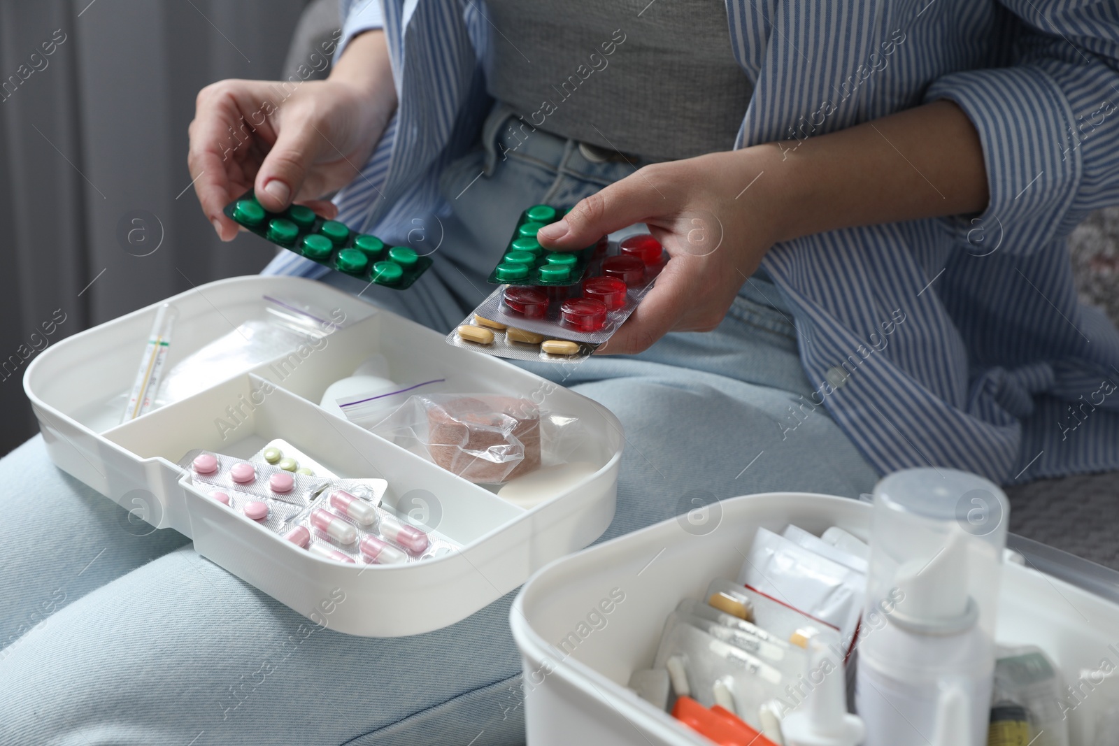 Photo of Woman putting pills into first aid kit indoors, closeup