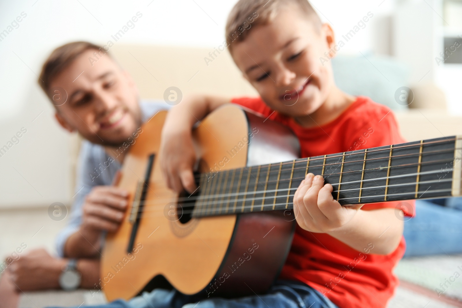 Photo of Father teaching his little son to play guitar at home