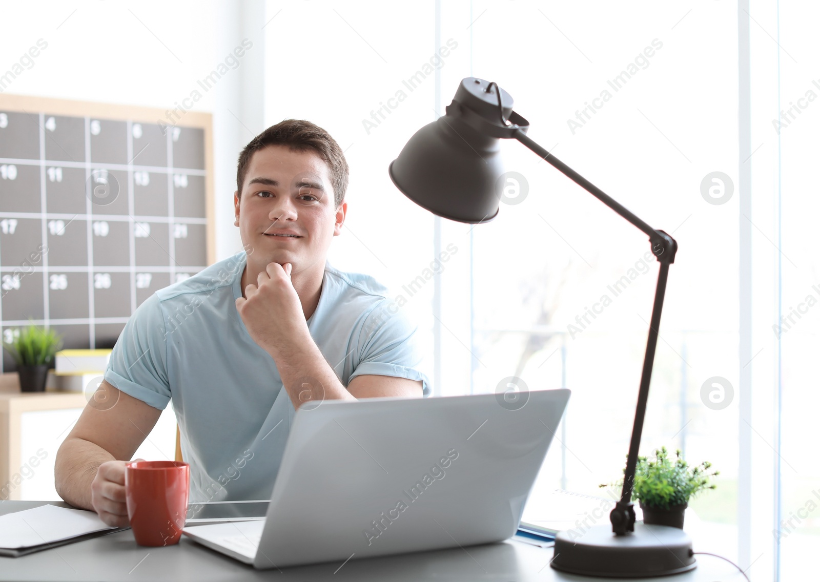 Photo of Portrait of confident young man with  laptop and cup at table