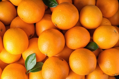 Photo of Pile of fresh ripe oranges with leaves as background, top view