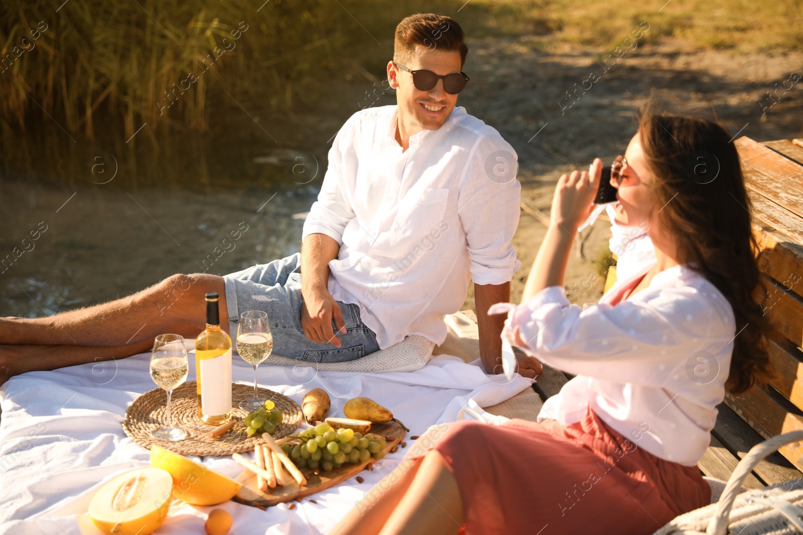 Photo of Woman taking picture of boyfriend on pier at picnic